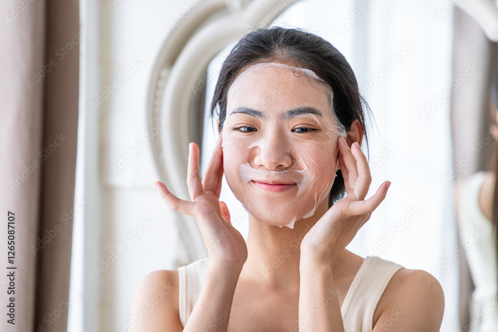 Naklejka premium Young Asian woman applying facial sheet mask for skincare routine
