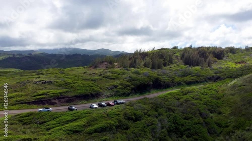 Zooming out drone shot of the majestic Hawaiian cliffs along Kahekili Highway near nakalele blowhole, Maui, revealing vast coastline, rugged landscape, and a parked car, all set Pacific Ocean photo