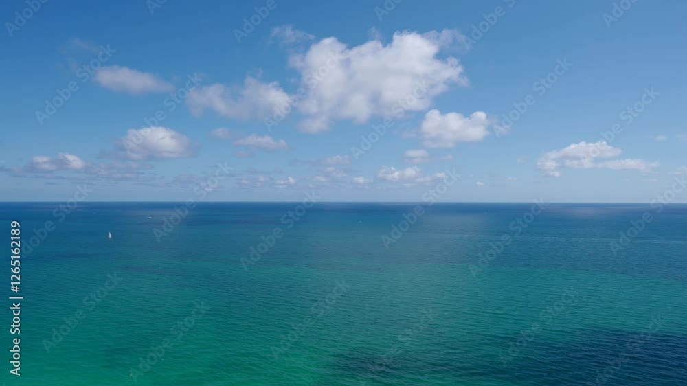 Serene ocean view with clear blue sky and scattered clouds. Water is gradient of turquoise near shore to deeper blue further out Serene ocean view with clear blue sky and scattered clouds. Water is gradient of turquoise near shore to deeper blue further out