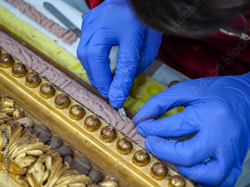 Close-up of a gold leaf frame restored by a male professional with latex gloves. Zenithal view