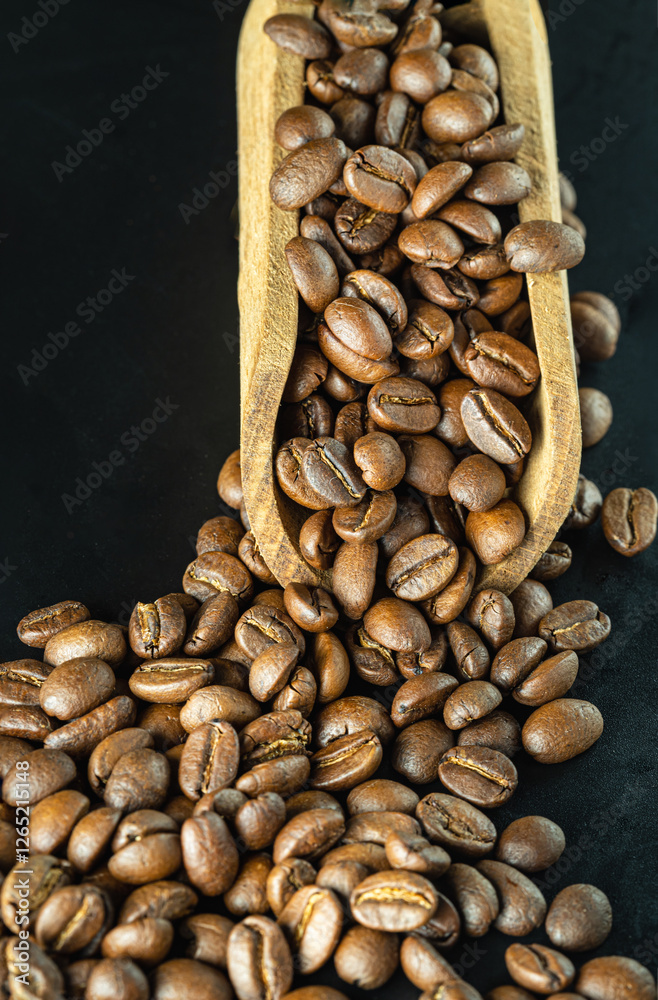 View of Roasted coffee beans on a rich textured surface in Wooden coffee scoop on Black background. Enjoy your morning coffee for living, use it as your Copy space, Design, Wallpaper and Poster.
