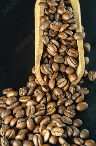 Obraz na płótnie View of Roasted coffee beans on a rich textured surface in Wooden coffee scoop on Black background. Enjoy your morning coffee for living, use it as your Copy space, Design, Wallpaper and Poster. w salonie