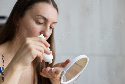 Woman in front of the mirror taking cream of from a tube. photo