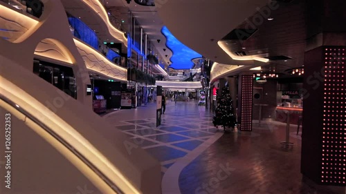 A stylish onboard view of MSC World Europa, featuring futuristic architecture, illuminated walkways, and elegant design. The ship’s shopping and dining area is decorated for the holiday season.