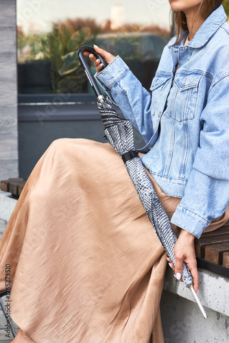 Obraz na płótnie Woman in casual denim jacket and skirt holding patterned closed umbrella on bench, style concept w salonie