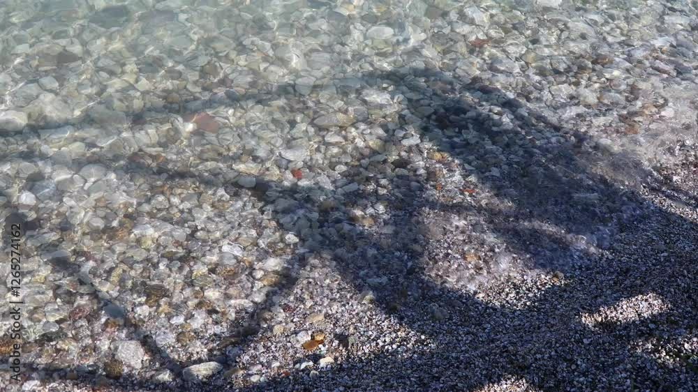 Shadows dance over the crystal-clear waters of Lake Garda in Sirmione, reflecting sunlight on smooth pebbles in Italy Shadows dance over the crystal-clear waters of Lake Garda in Sirmione, reflecting sunlight on smooth pebbles in Italy