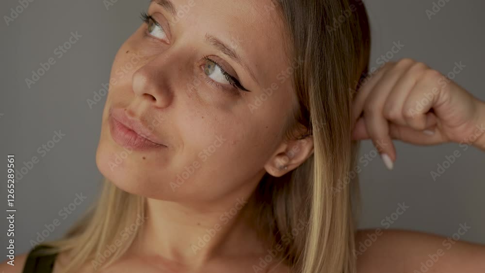 Young caucasian blonde woman showing arrow on the eyelid running her finger over her face on a dark grey background. A girl with a makeup Young caucasian blonde woman showing arrow on the eyelid running her finger over her face on a dark grey background. A girl with a makeup