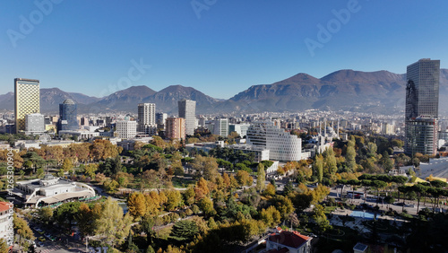 Bild auf Leinwand Aerial view of Tirana’s city center on a sunny day, showcasing Skanderbeg Square, modern high-rises, and historic landmarks, with Dajti Mountain in the background