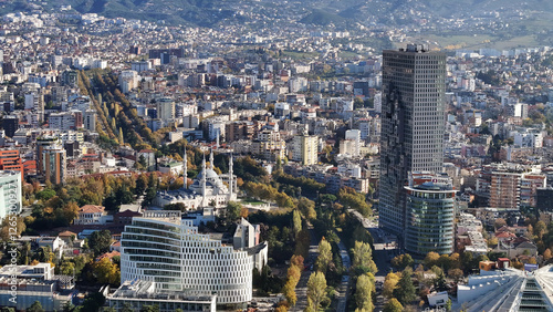 Fotografía Aerial view of Tirana’s city center on a sunny day, showcasing Skanderbeg Square, modern high-rises, and historic landmarks, with Dajti Mountain in the background
