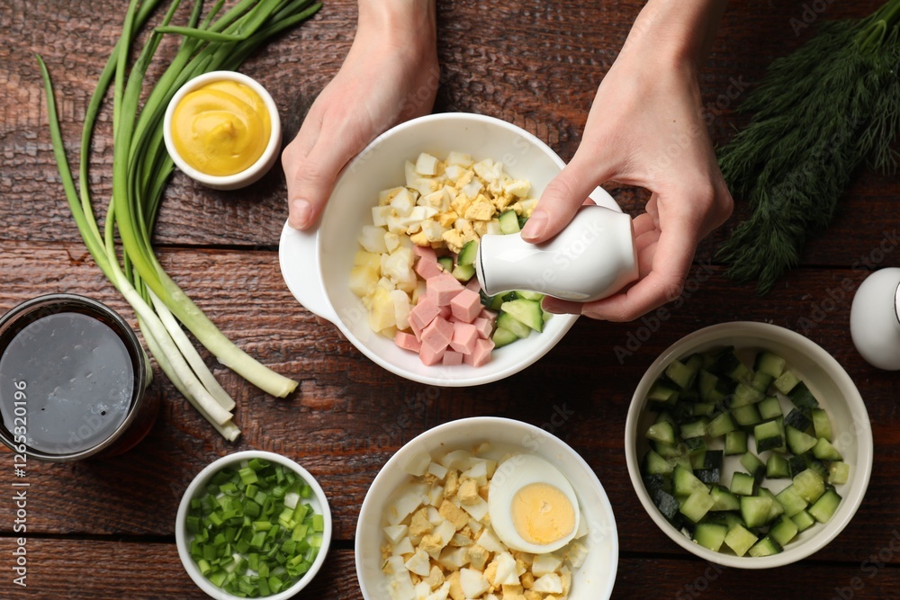 Making okroshka soup. Woman adding salt into bowl with different ingredients at wooden table, top view Making okroshka soup. Woman adding salt into bowl with different ingredients at wooden table, top view