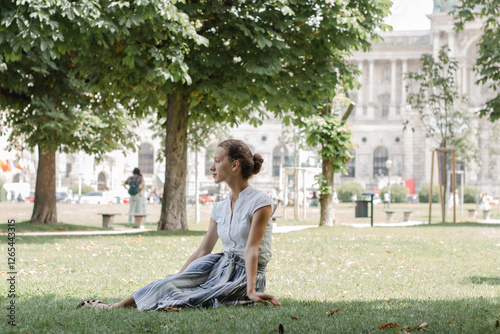 The girl sits thoughtfully on the grass in the park, dressed femininely and elegantly, looks sophisticated and looks away. photo