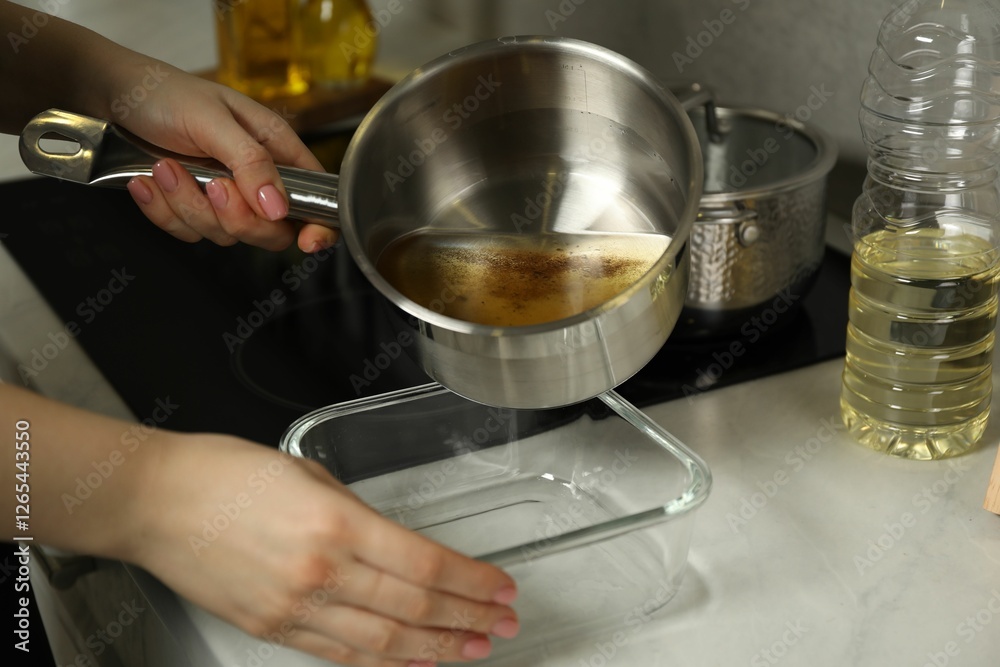 Woman pouring used cooking oil into glass container at white marble countertop, closeup Woman pouring used cooking oil into glass container at white marble countertop, closeup
