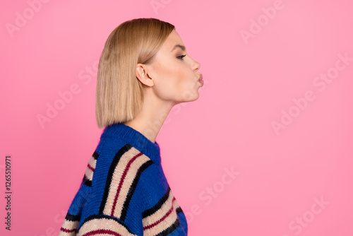 Side profile of a stylish young woman wearing a striped sweater puckering lips against a pink backdrop