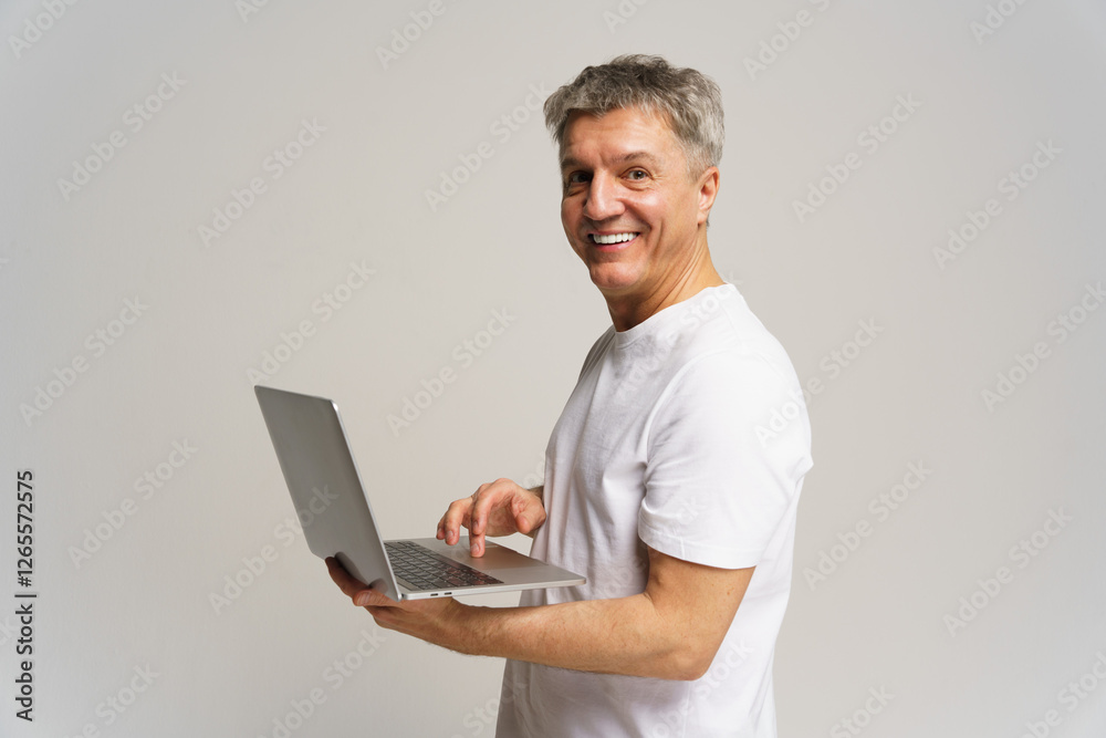 Older man smiling while using laptop in studio with neutral background Older man smiling while using laptop in studio with neutral background