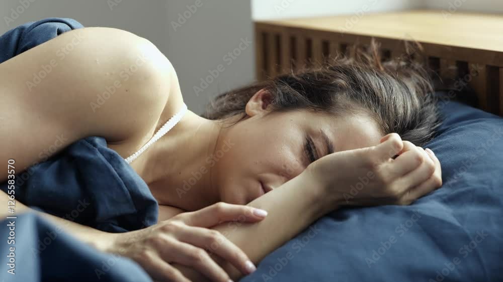 Young woman stay at home during quarantine. Unhappy unpleasant girl lying on bed and cover face from noise or morning light. Time to wake up. Young woman stay at home during quarantine. Unhappy unpleasant girl lying on bed and cover face from noise or morning light. Time to wake up.