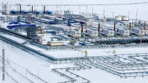 Snowy landscape enveloping industrial gas processing facility, highlighting intricate pipeline network and massive storage tanks against stark arctic winter backdrop. Gas production concept in Russia
