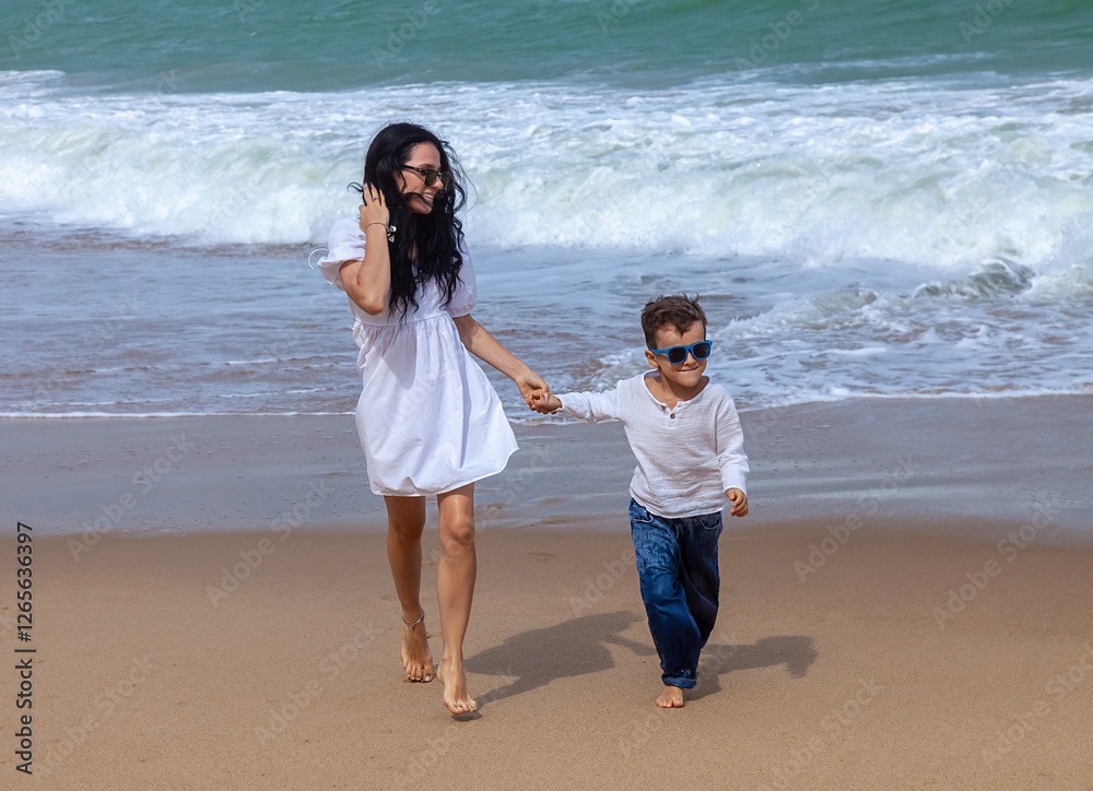 A woman and a child are walking on the beach. The woman is holding the child's hand