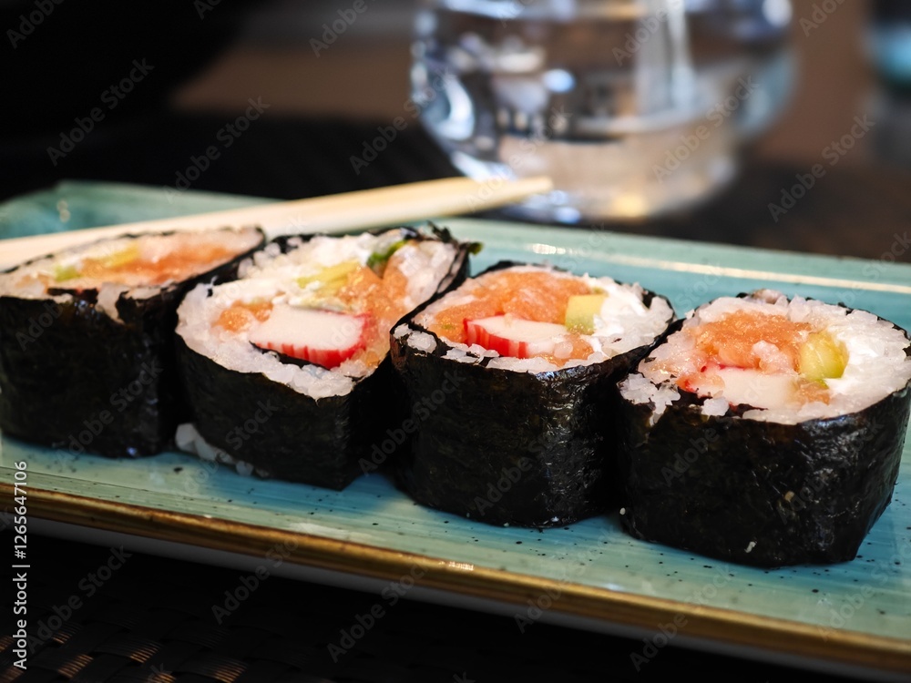 Sushi rolls arranged neatly on a blue plate with water in the background, creating a delightful dining moment Sushi rolls arranged neatly on a blue plate with water in the background, creating a delightful dining moment