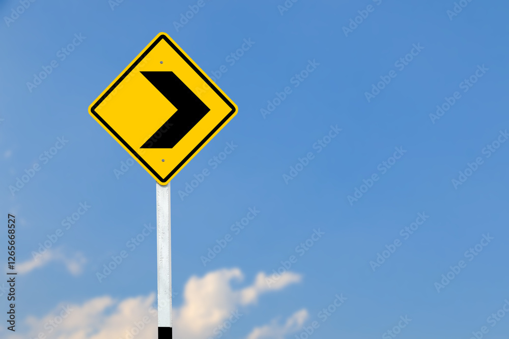 Black right direction symbol is displayed on a bright yellow traffic sign on blurred sky background. Black right direction symbol is displayed on a bright yellow traffic sign on blurred sky background.