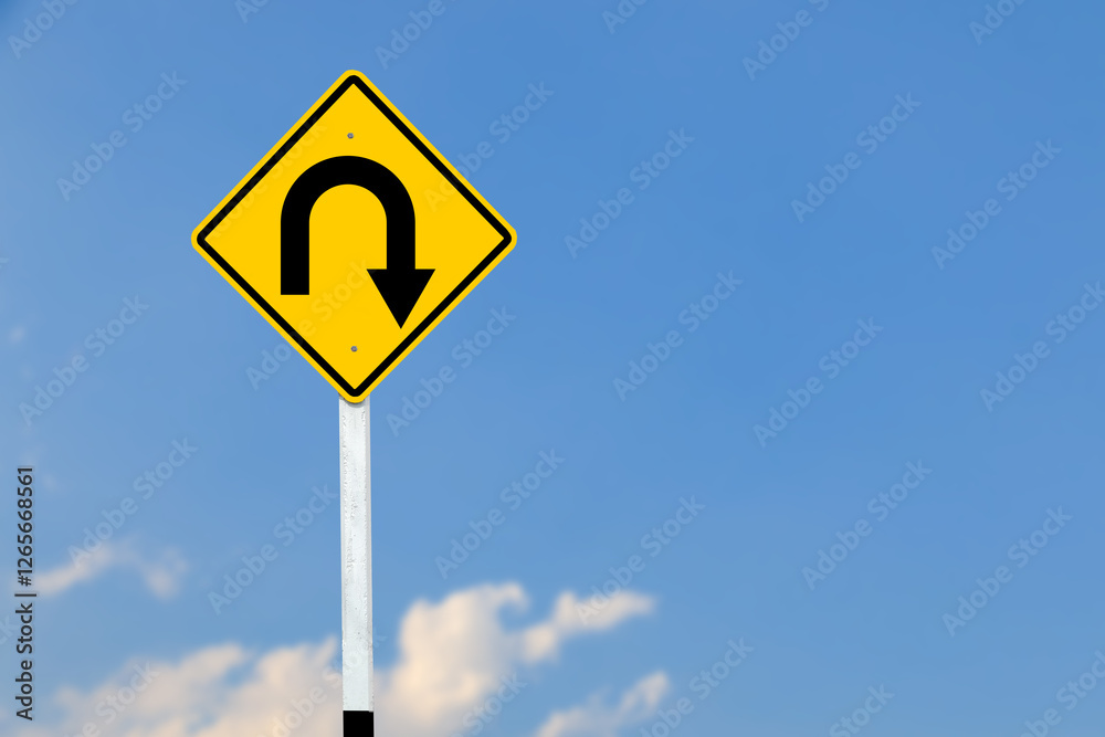 A black U turn symbol is prominently displayed on a bright yellow sign on blurred sky background. A black U turn symbol is prominently displayed on a bright yellow sign on blurred sky background.
