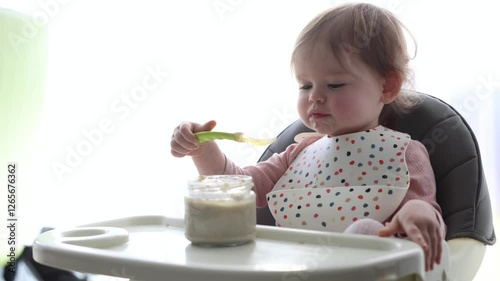 A Playful Baby is Happily Enjoying Food with a Spoon in a Colorful Bowl During Mealtime