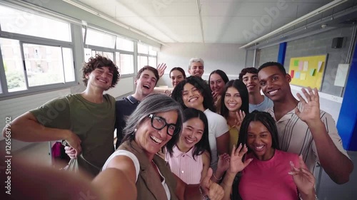 Cheerful selfie of young group of students waving and looking at camera with big smiles with their female teacher in the classroom, celebrating the back to school.