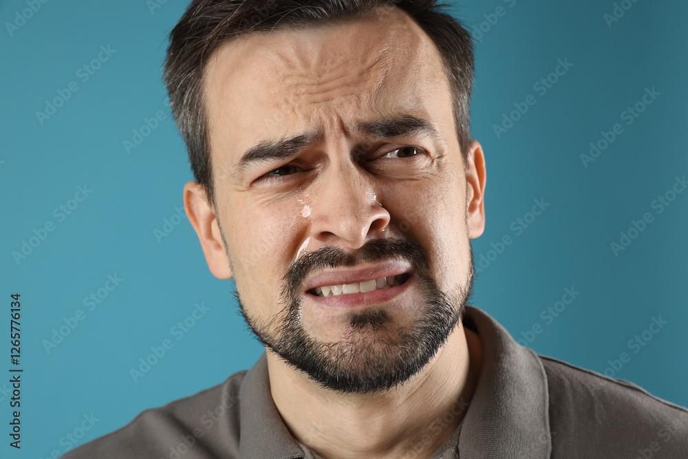 Obraz premium Sad man crying on light blue background, closeup