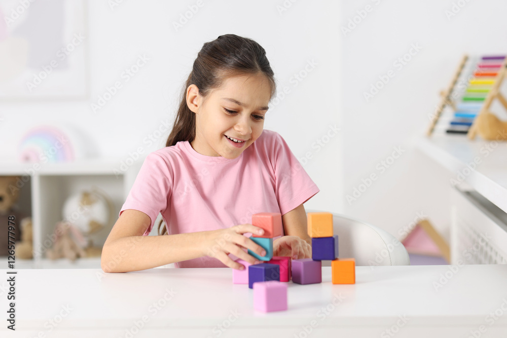 Happy girl building pyramid of colorful cubes at table indoors Happy girl building pyramid of colorful cubes at table indoors