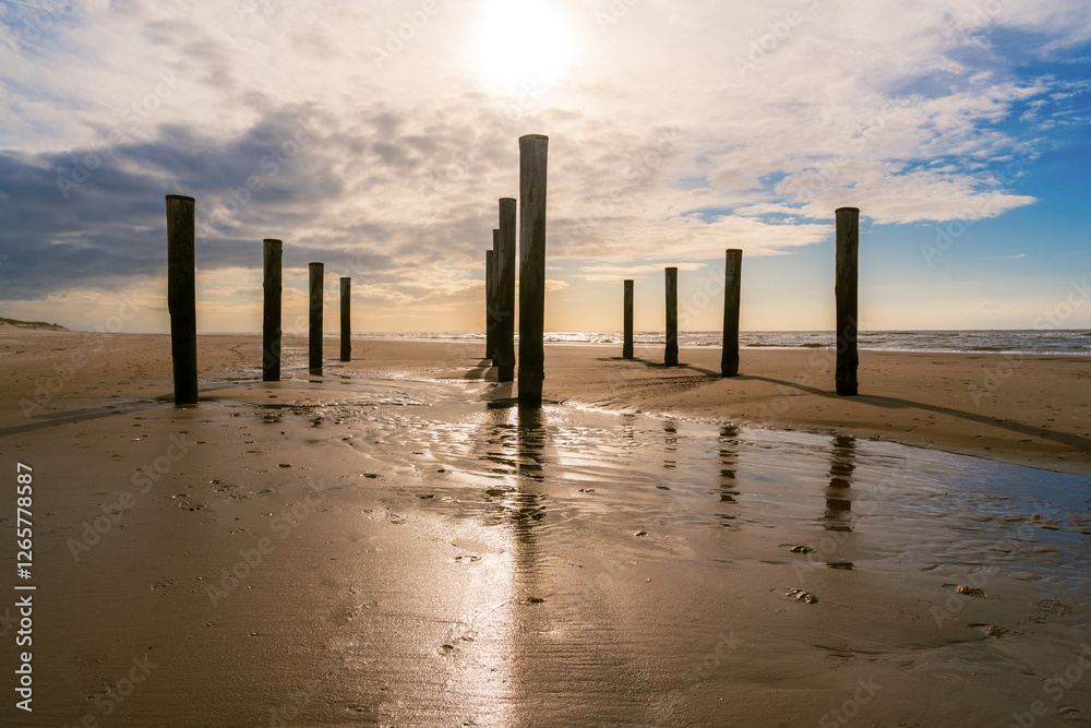 Sandstrand mit Holzpfählen und blauem Himmel mit Wolken