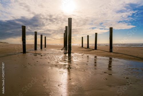 Obraz na płótnie Sandstrand mit Holzpfählen und blauem Himmel mit Wolken w salonie