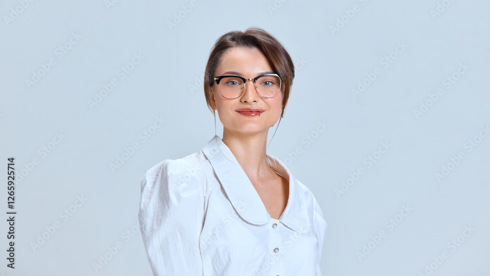 Close up of young woman with calm expression wearing glasses, dressed in white blouse, standing straight against white background. Concept of professionalism, influence, business mindset Close up of young woman with calm expression wearing glasses, dressed in white blouse, standing straight against white background. Concept of professionalism, influence, business mindset