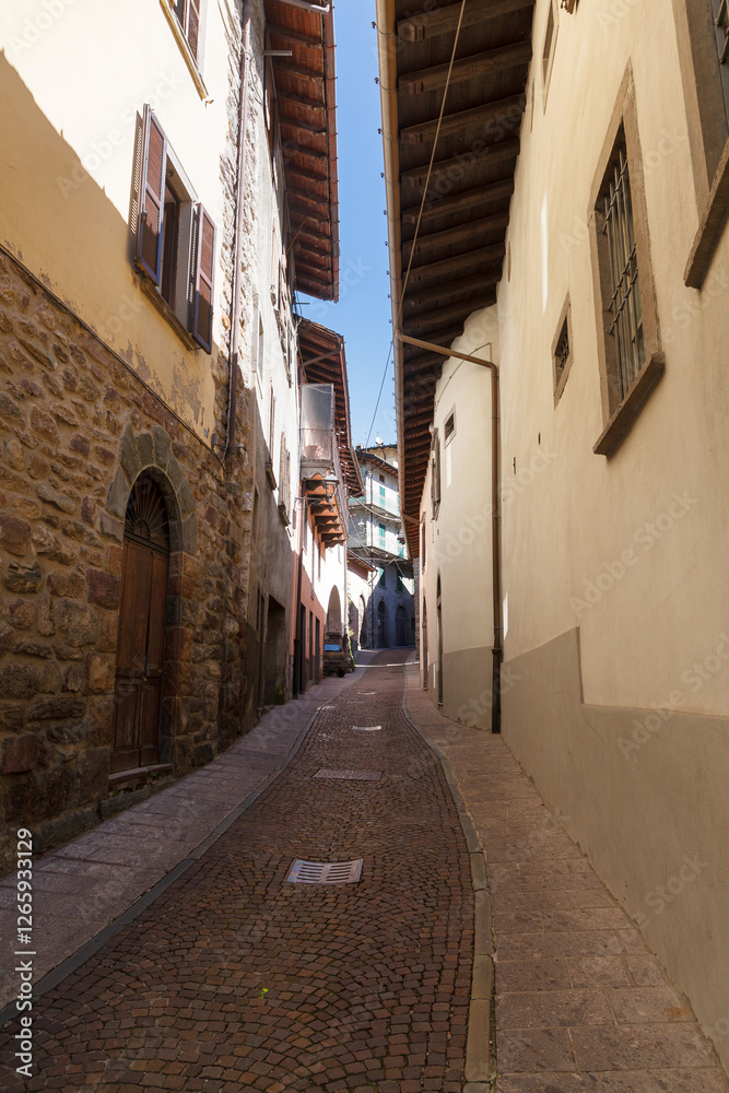 Street view of historical village Gromo, Bergamo, Lombardy, Italy. Narrow cobbled streets. Sun lights and shadows.