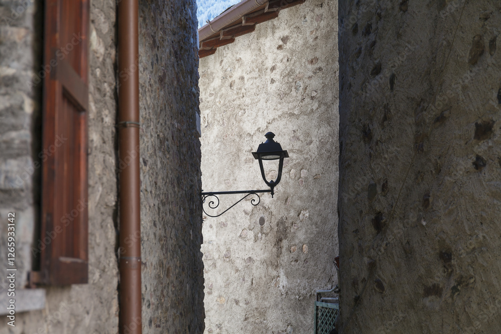 A vintage street lamp attached to a rustic stone wall of narrow old town street, featuring detailed ironwork and a weathered charm.