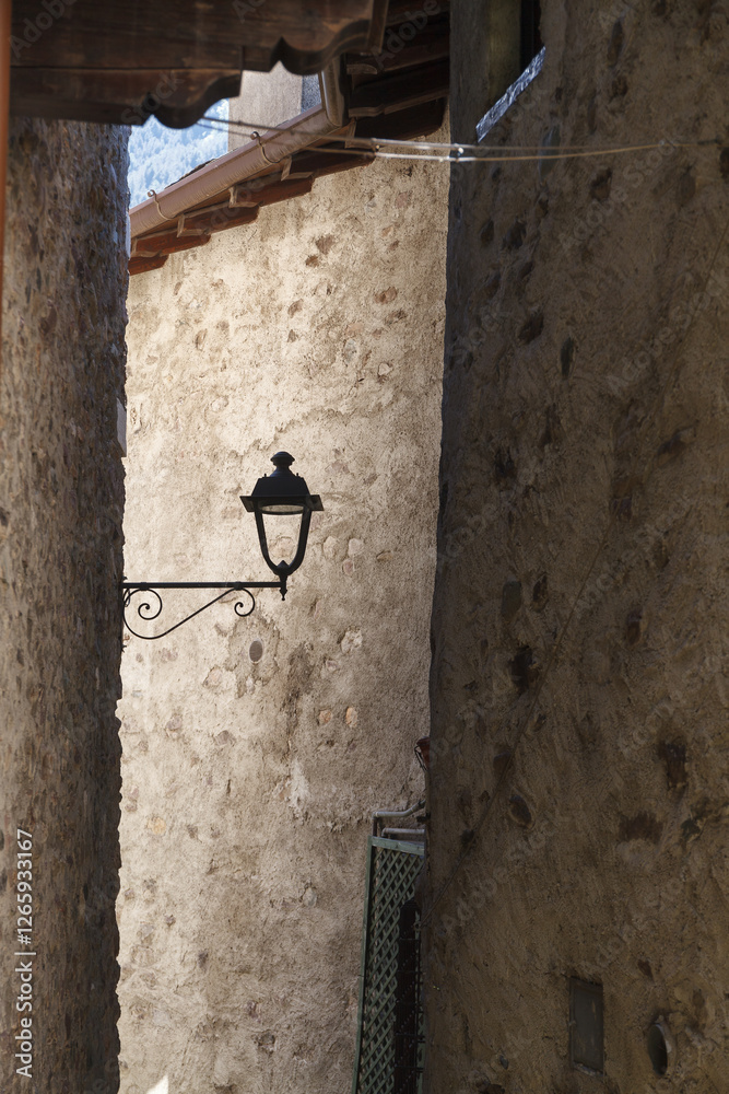 A vintage street lamp attached to a rustic stone wall of narrow old town street, featuring detailed ironwork and a weathered charm.