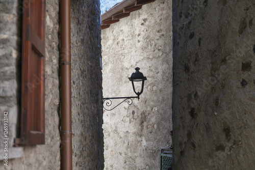Obraz na płótnie A vintage street lamp attached to a rustic stone wall of narrow old town street, featuring detailed ironwork and a weathered charm. w salonie