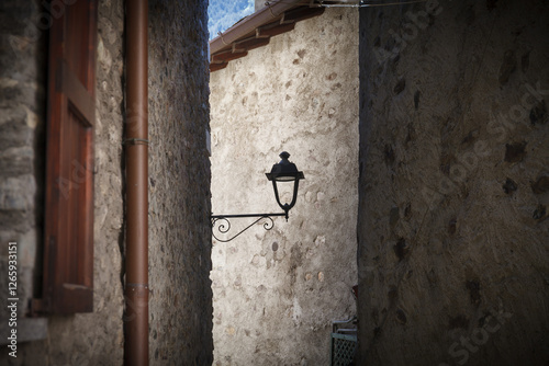 Obraz na płótnie A vintage street lamp attached to a rustic stone wall of narrow old town street, featuring detailed ironwork and a weathered charm. w salonie