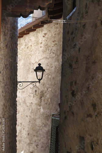 Obraz na płótnie A vintage street lamp attached to a rustic stone wall of narrow old town street, featuring detailed ironwork and a weathered charm. w salonie