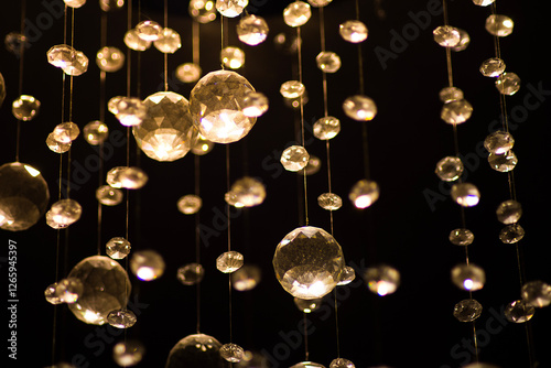 Close-up of sparkling crystal decorations hanging in a dark setting, illuminated by warm golden light. The elegant and luxurious details create a mesmerizing and dreamy ambiance.


