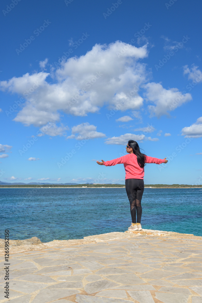 beautiful latina woman standing near the ocean with arms open, enjoying the calm, dressed in pink and black beautiful latina woman standing near the ocean with arms open, enjoying the calm, dressed in pink and black