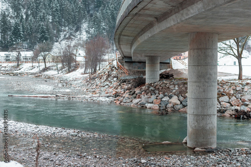 Obraz na płótnie Concrete Bridge with metal railing is visible crossing the river and snow capped hills with forest seen in the background. Detail on big concrete pillar w salonie