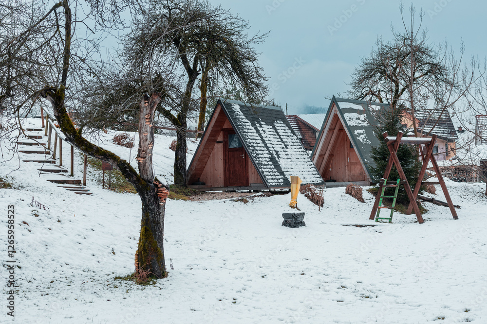 Small wooden houses, glamping like setting with childrens playground outside, covered in snow in winter time