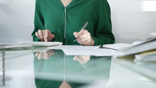 Bilde på lerret Businesswoman accountant at a sleek glass desk in a contemporary office, using a calculator to crunch numbers and jotting down meticulous notes, green color style