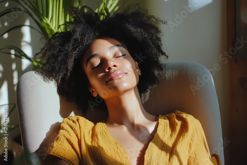 Young woman relaxing in sunlight with natural hair while sitting in a cozy ch...
