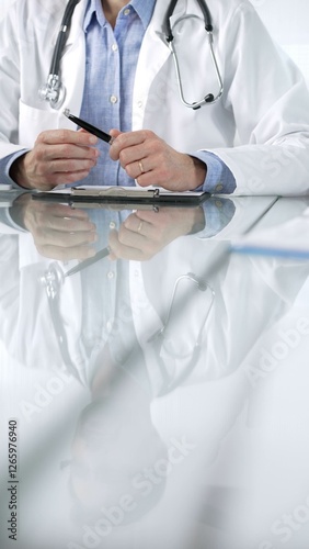 Obraz na płótnie Unknown male doctor wearing a stethoscope, blue shirt and a lab coat is gesturing with hands overs a glass desk with laptop in clinic office, vertical closeup view. Medicine concept w salonie
