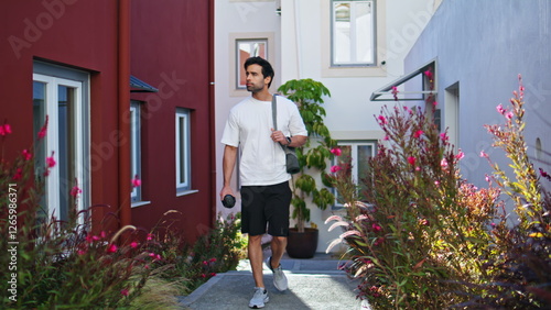 Sporty man walking outdoors with fitness gear surrounded by flowers and greenery photo