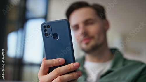 Blurred guy looking mobile phone receiving message notification at home closeup
