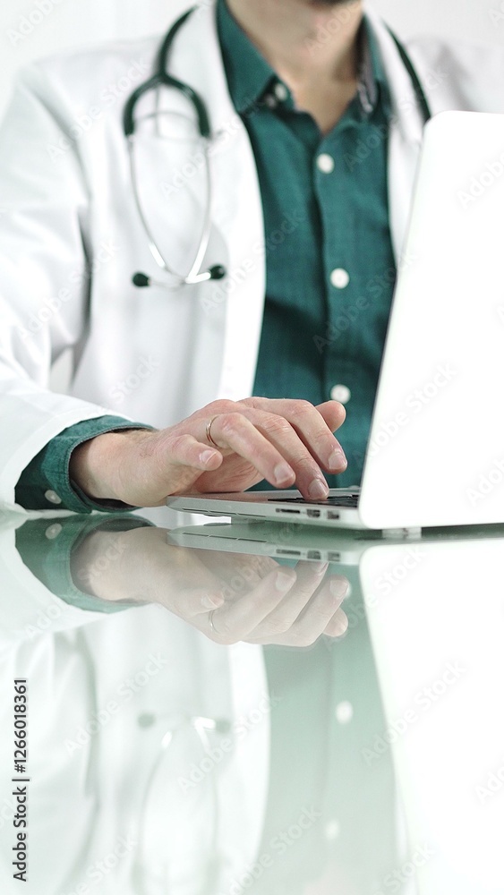 Doctor man in a green shirt under a medical coat is using technology in medicine. Close-up of hands typing on a laptop on a glass desk in the clinic, vertical view. Healthcare concept Doctor man in a green shirt under a medical coat is using technology in medicine. Close-up of hands typing on a laptop on a glass desk in the clinic, vertical view. Healthcare concept