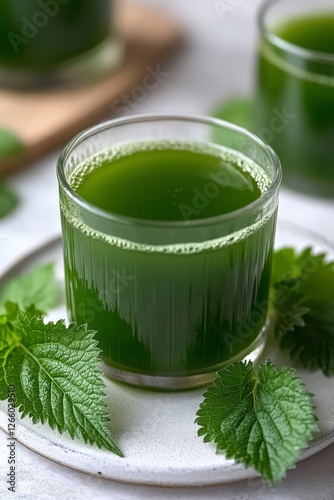 A glass of freshly made nettle juice sits on a light-colored plate, surrounded by green nettle leaves