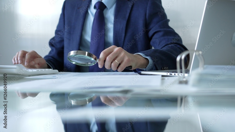 Businessman analyzing financial data with magnifying glass and calculator, conducting audit or review in office. Audit and taxes theme in business