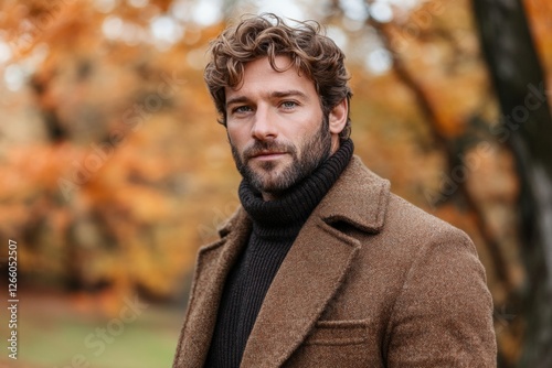 Stylish man in a brown coat poses in autumn park surrounded by colorful foliage